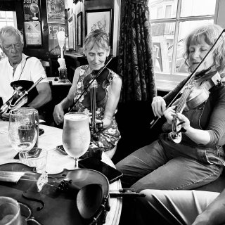 A piper and two women fiddlers at a pub table with another fiddle on it.