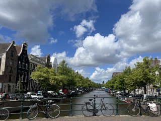 Bicycles on a bridge over a tree-lined canal under a blue sky with greyish white clouds.