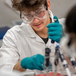 man using pipette in lab coat and safety goggles