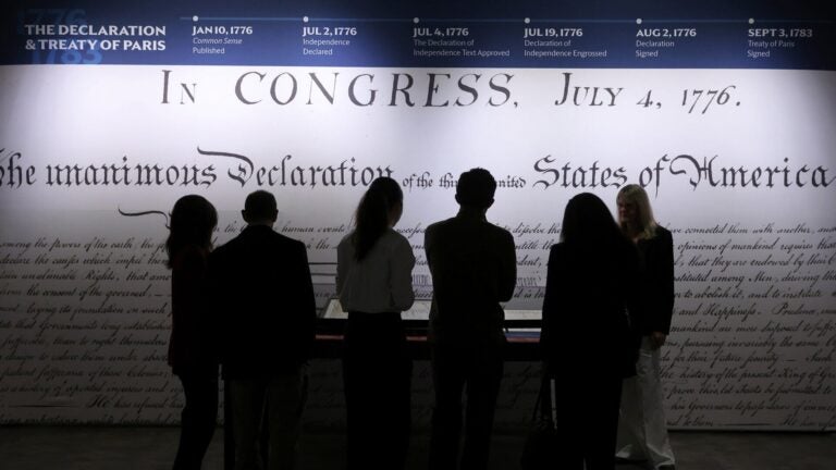 People in silhoutte stand and view a wall displaying the Declaration of Independence
