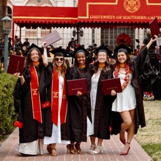 A group of graduates pose together in their caps and gowns on campus at commencement.