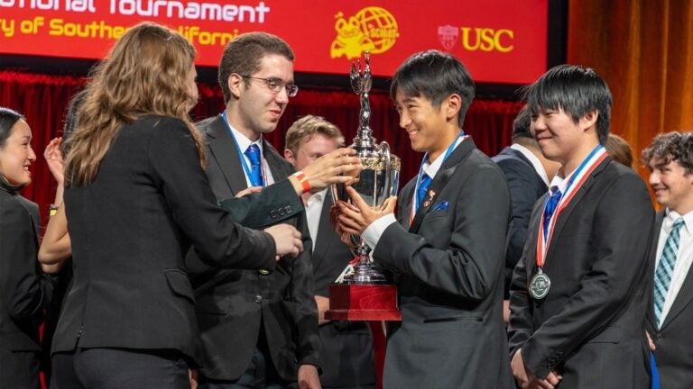Students wearing medals hold a trophy on stage.