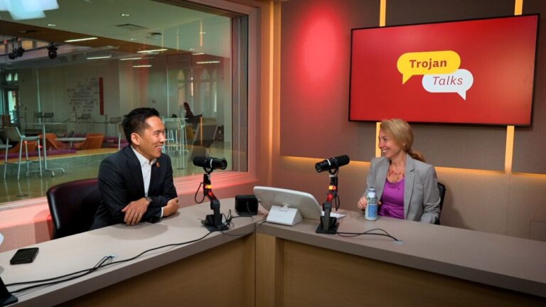 A man and woman in a sound booth with a monitor displaying 