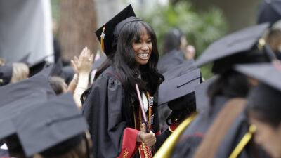 Image of graduate standing up and smiling surrounded by other graduates.