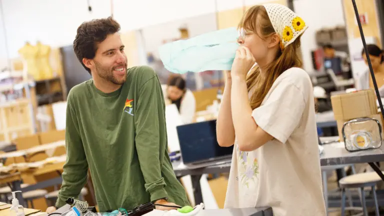 Two students in electrical engineering lab with soldering equipment blowing air into a bag.