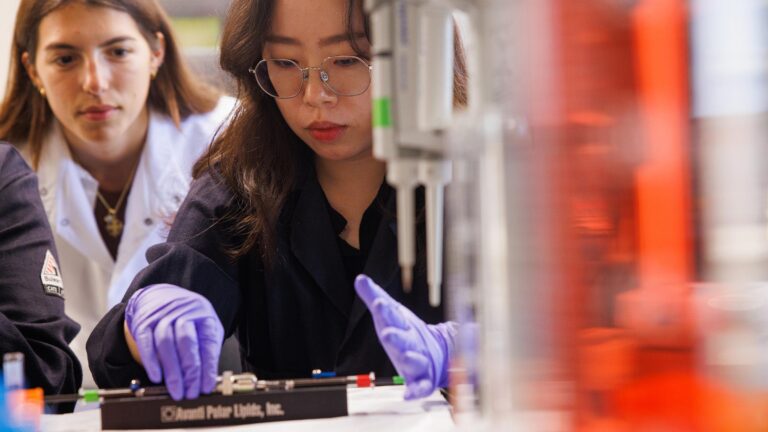 Student completes science experiment in lab as the instructor watches their work.