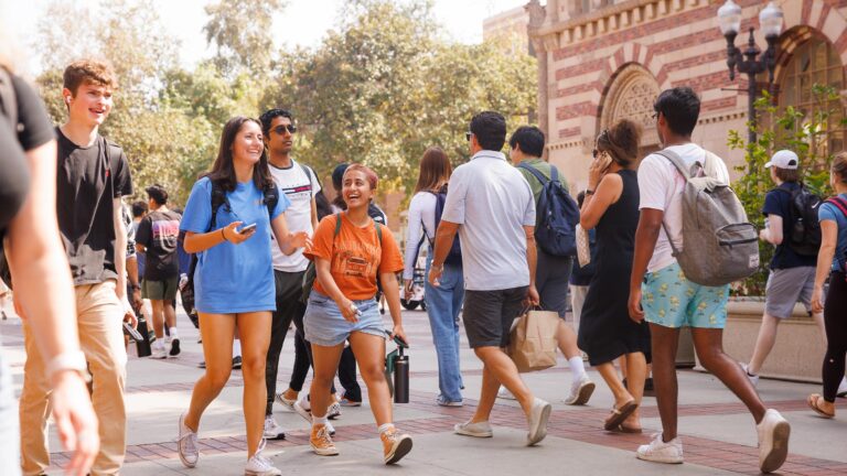 Two students walking through the walkway near Ronald Tutor Center on a busy day as other students walk around them.