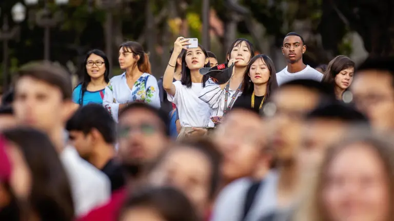 USC students gather at a Welcome Event and hold up their phones to take a picture of the event.