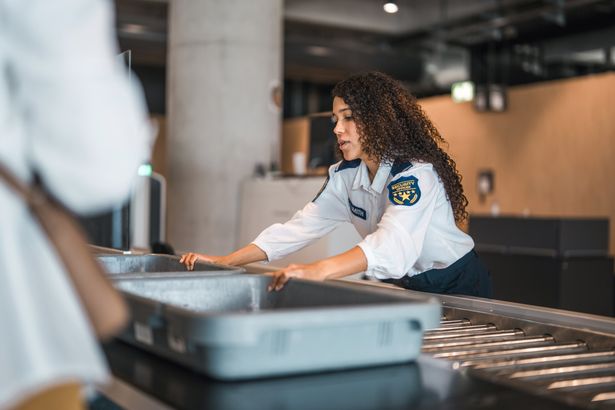 female airport security officer in uniform assists passengers at a luggage screening station, ensuring safety